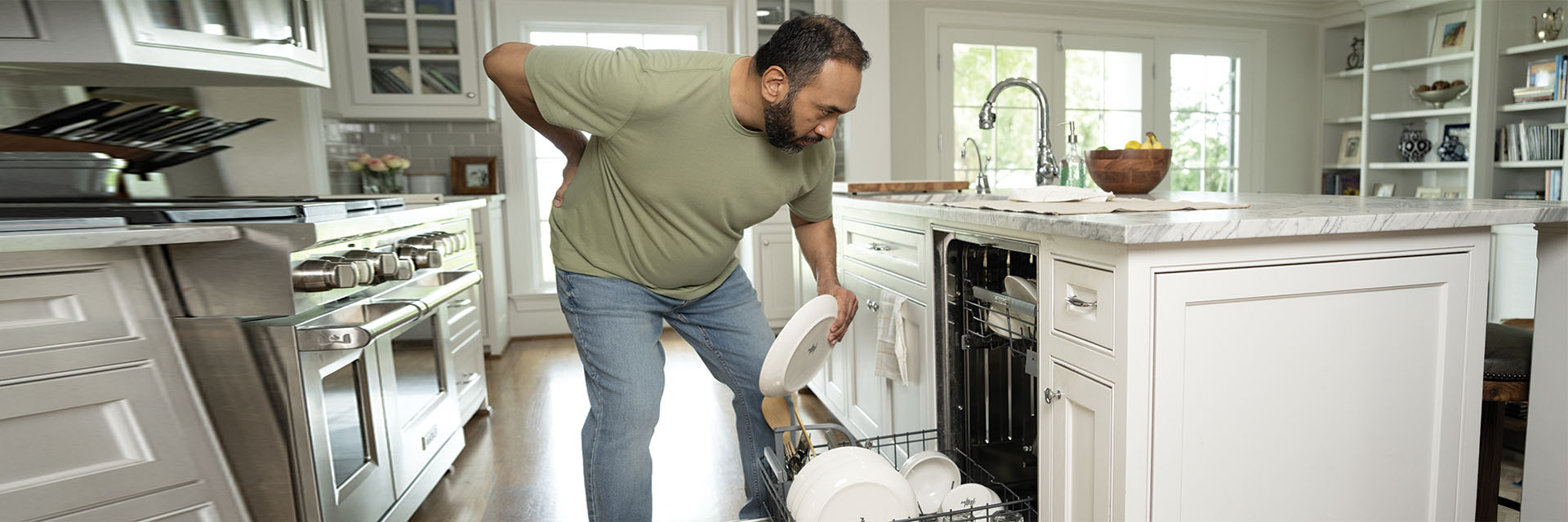 Man experiencing back pain while putting away dishes